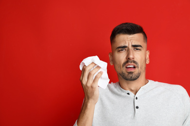 Man sneezing on red background, space for text. Cold symptoms
