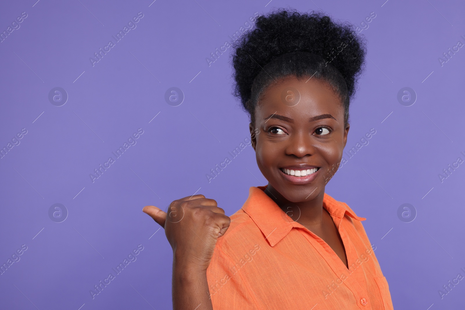 Photo of Happy young woman pointing at something on purple background. Space for text