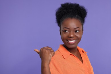 Photo of Happy young woman pointing at something on purple background. Space for text