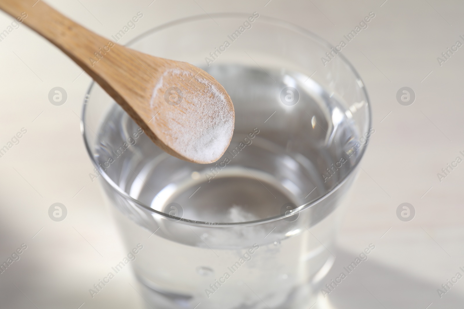 Photo of Adding baking soda into glass of water on light background, closeup