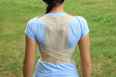 Photo of Closeup of woman with orthopedic corset on green grass outdoors, back view