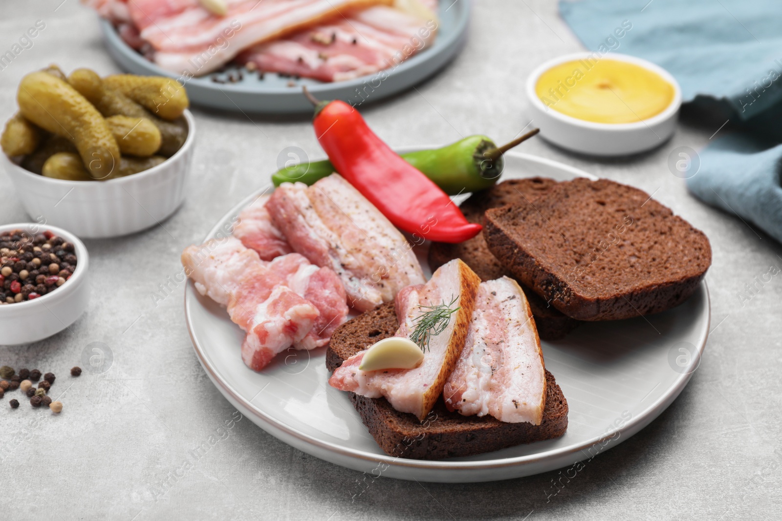 Photo of Tasty pork fatback with rye bread and spices on grey table