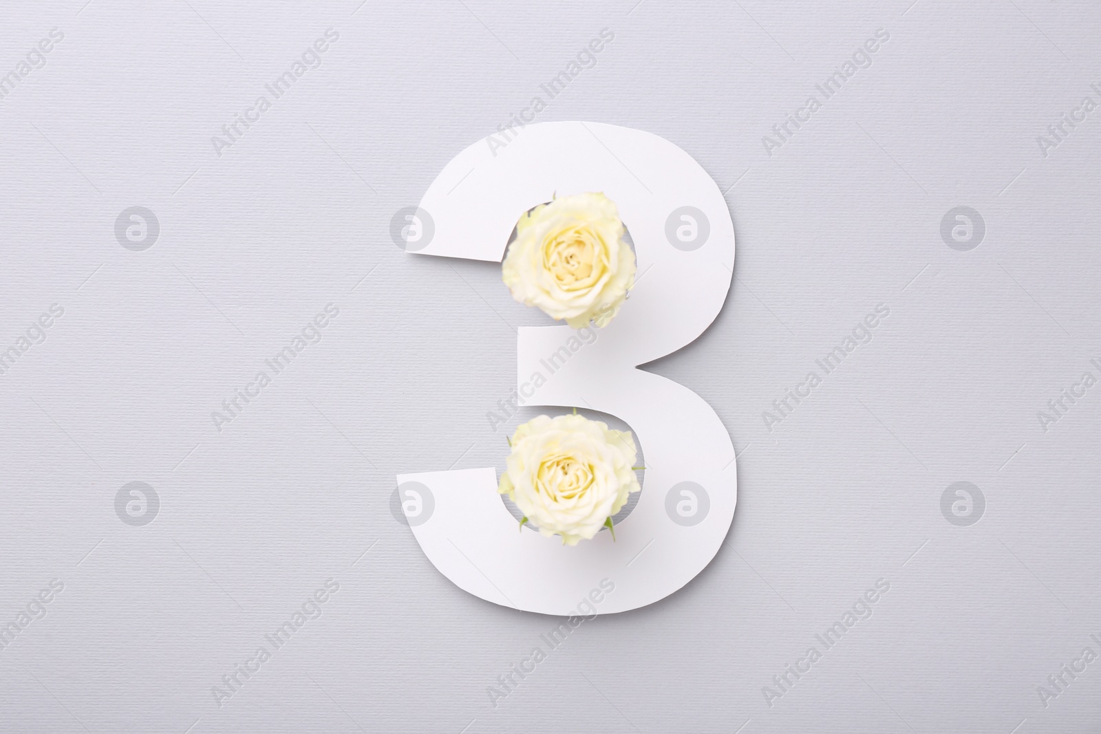 Photo of Paper number 3 and beautiful rose flowers on light grey background, top view