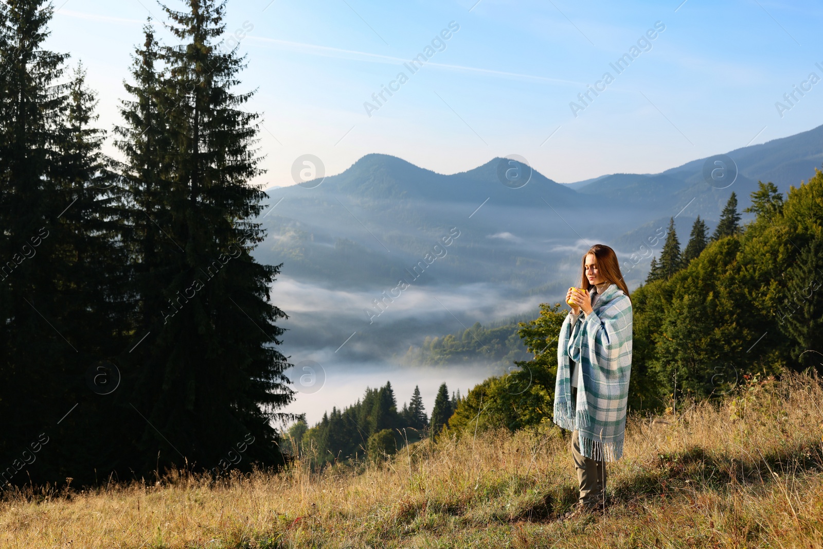 Photo of Woman with cozy plaid enjoying cup of hot beverage in mountains