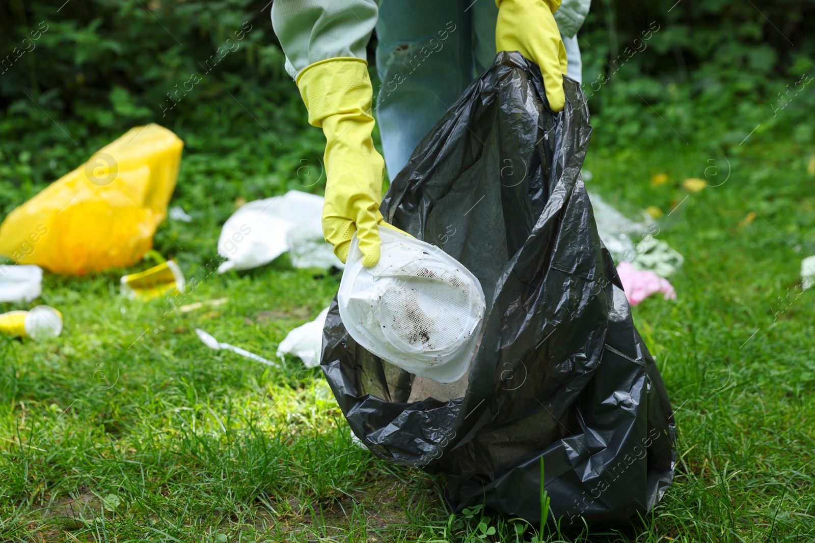 Photo of Woman with plastic bag collecting garbage on green grass outdoors, closeup