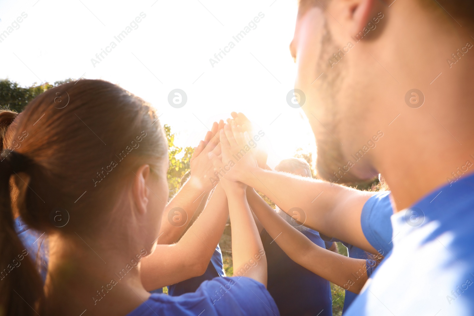 Photo of Group of volunteers joining hands together outdoors on sunny day