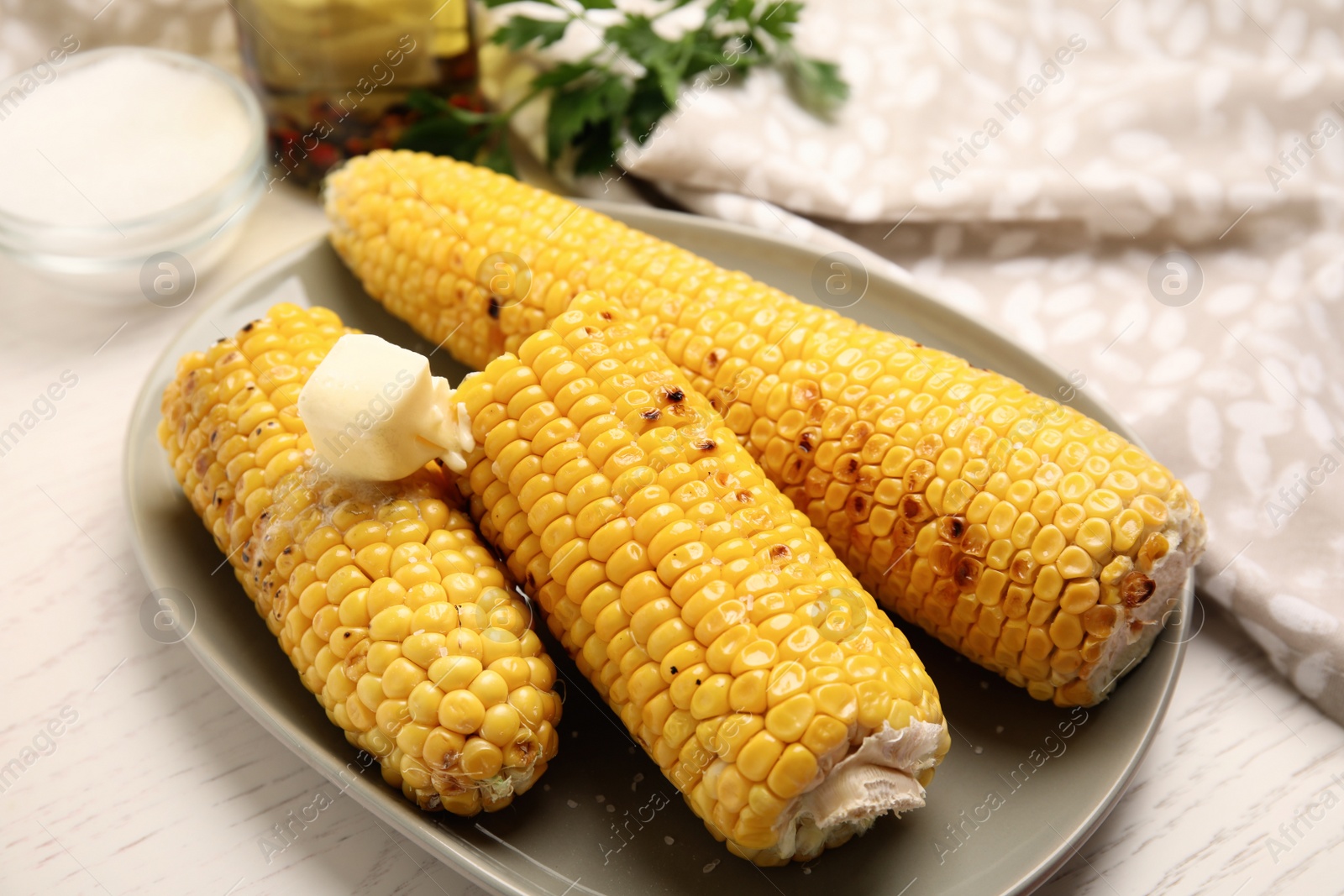 Photo of Fresh grilled corn cobs with butter on white wooden table, closeup