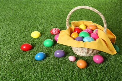 Photo of Wicker basket with Easter eggs on green grass. Space for text