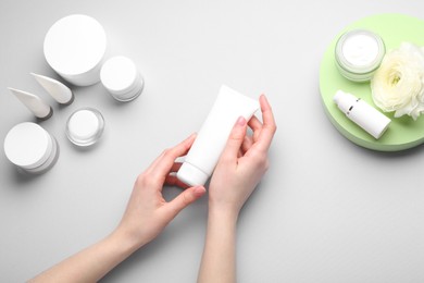 Woman holding tube of cream on light background, top view