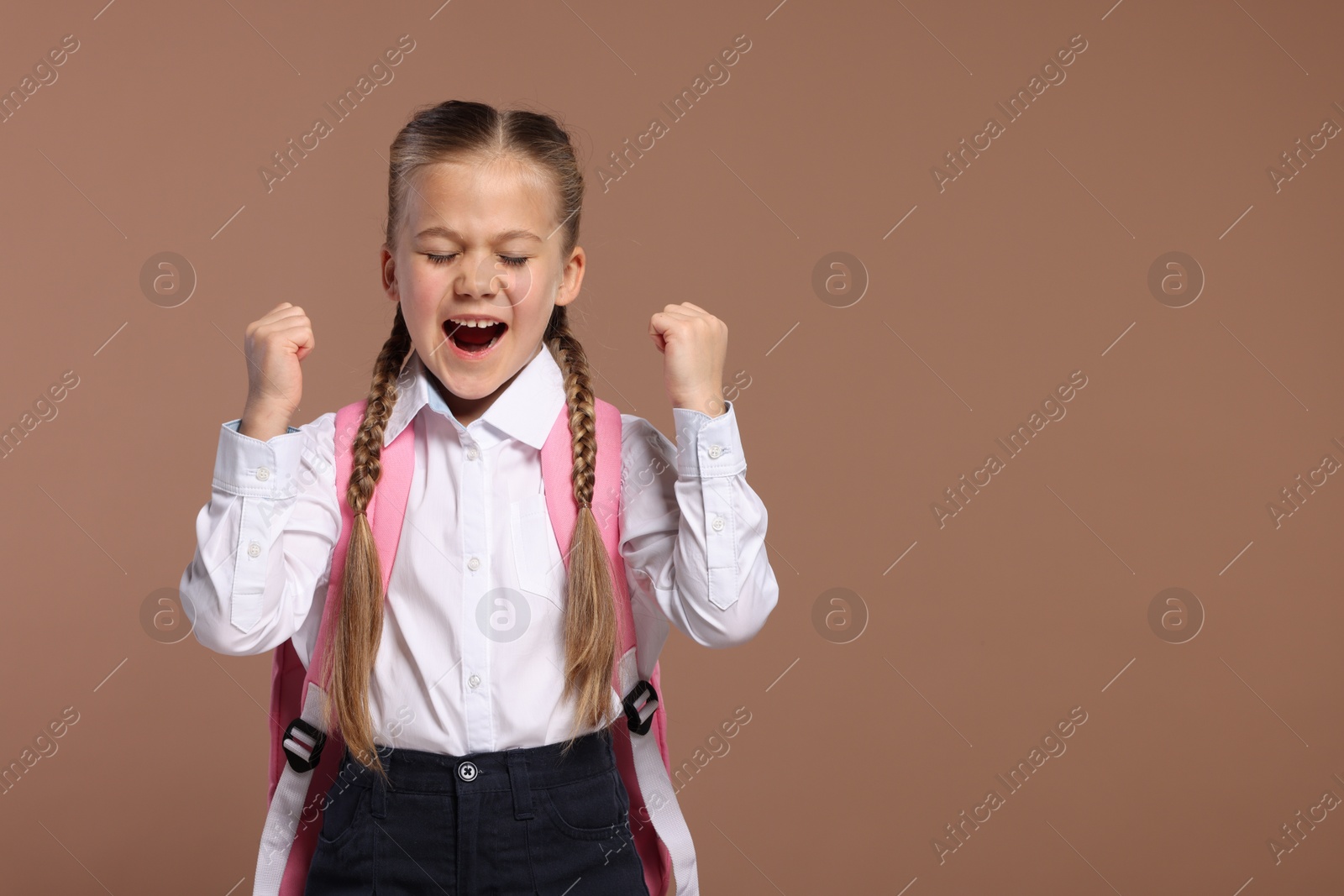 Photo of Emotional schoolgirl with backpack on brown background, space for text