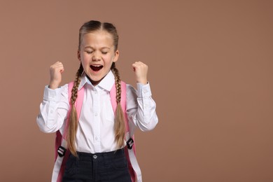 Emotional schoolgirl with backpack on brown background, space for text