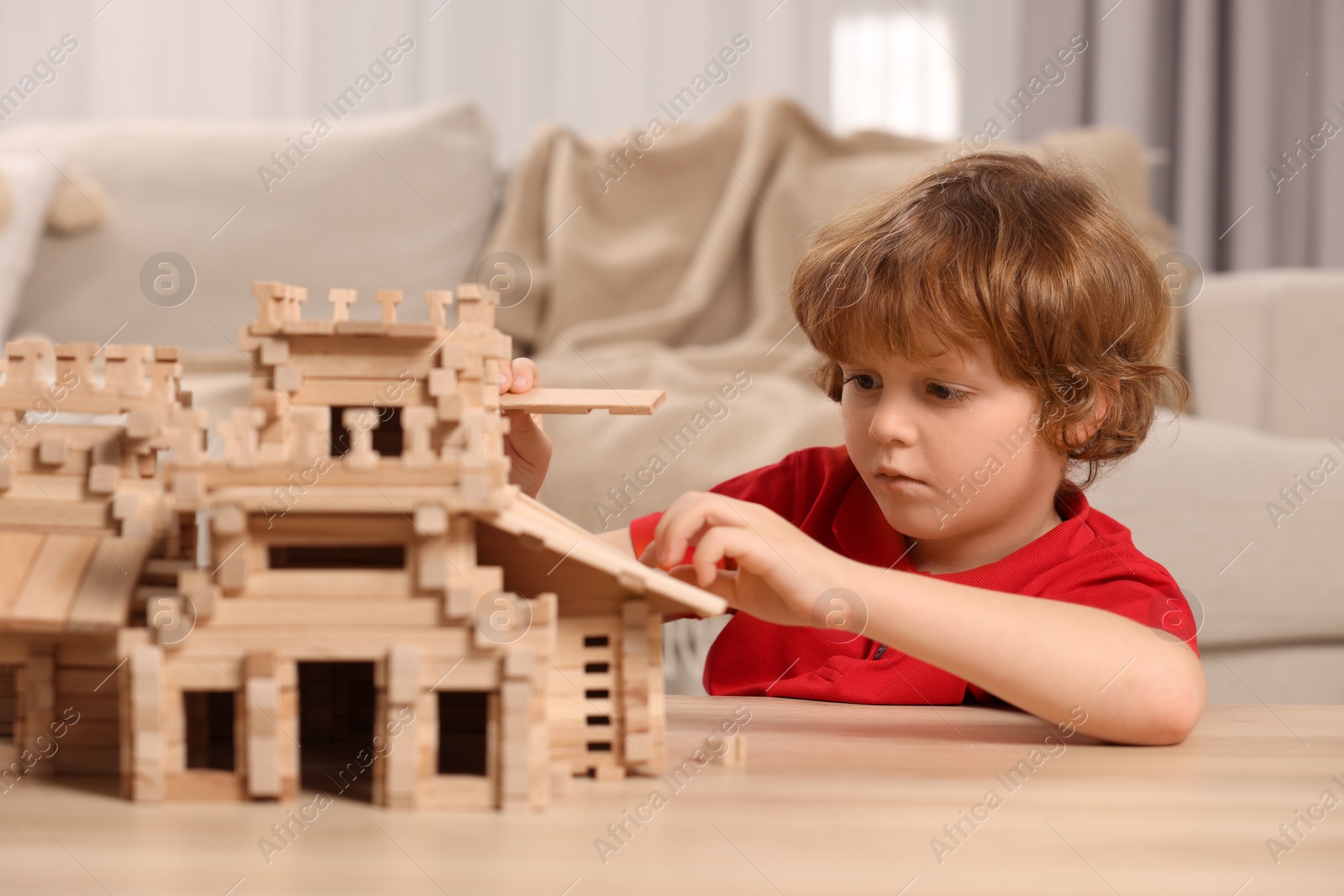 Photo of Cute little boy playing with wooden castle at table in room. Child's toy