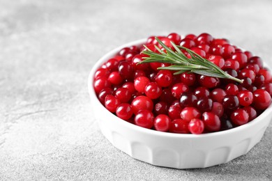 Photo of Fresh ripe cranberries and rosemary in bowl on grey table, closeup. Space for text