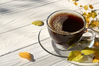 Cup of hot drink and leaves on white wooden table, closeup with space for text. Cozy autumn atmosphere