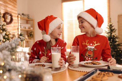 Photo of Cute little children with delicious Christmas cookies and milk at home