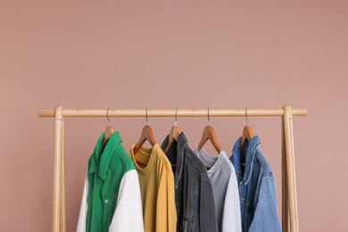 Rack with stylish clothes on wooden hangers against beige background