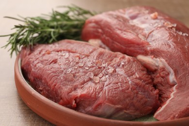 Pieces of raw beef meat with spices and rosemary on table, closeup