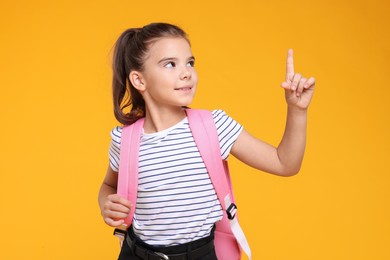 Photo of Cute schoolgirl pointing upwards on orange background