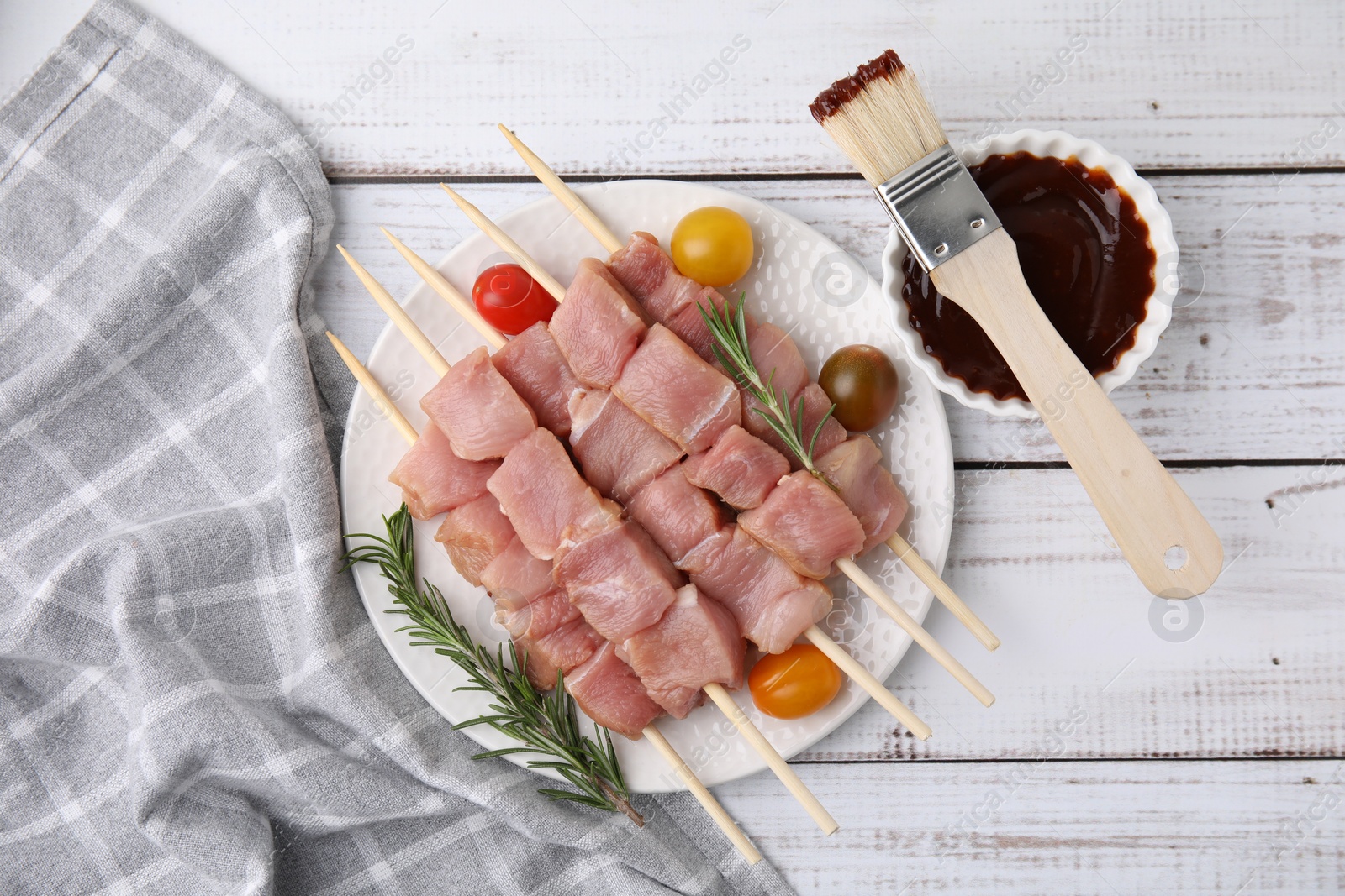 Photo of Skewers with pieces of raw meat, rosemary, tomatoes and marinade on rustic wooden table