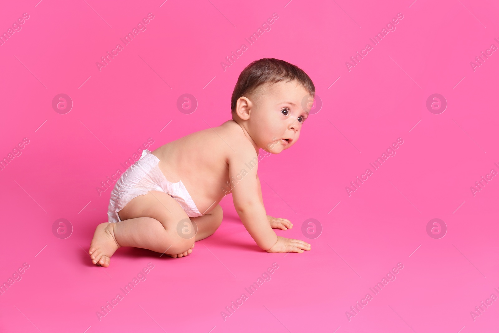 Photo of Cute baby in dry soft diaper crawling on pink background