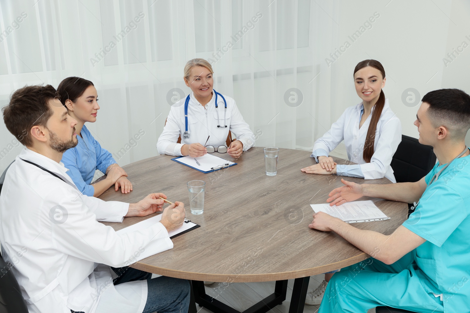 Photo of Medical conference. Team of doctors having discussion at wooden table in clinic