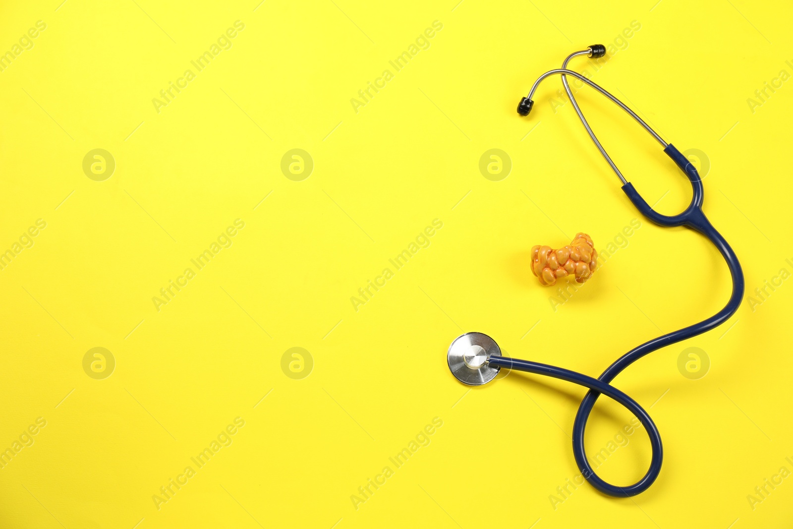 Photo of Endocrinology. Stethoscope and model of thyroid gland on yellow background, top view. Space for text