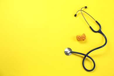 Endocrinology. Stethoscope and model of thyroid gland on yellow background, top view. Space for text