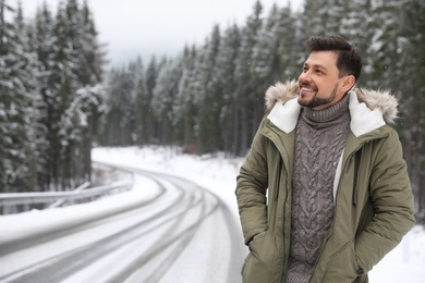 Man in warm clothes near snowy forest, space for text. Winter vacation