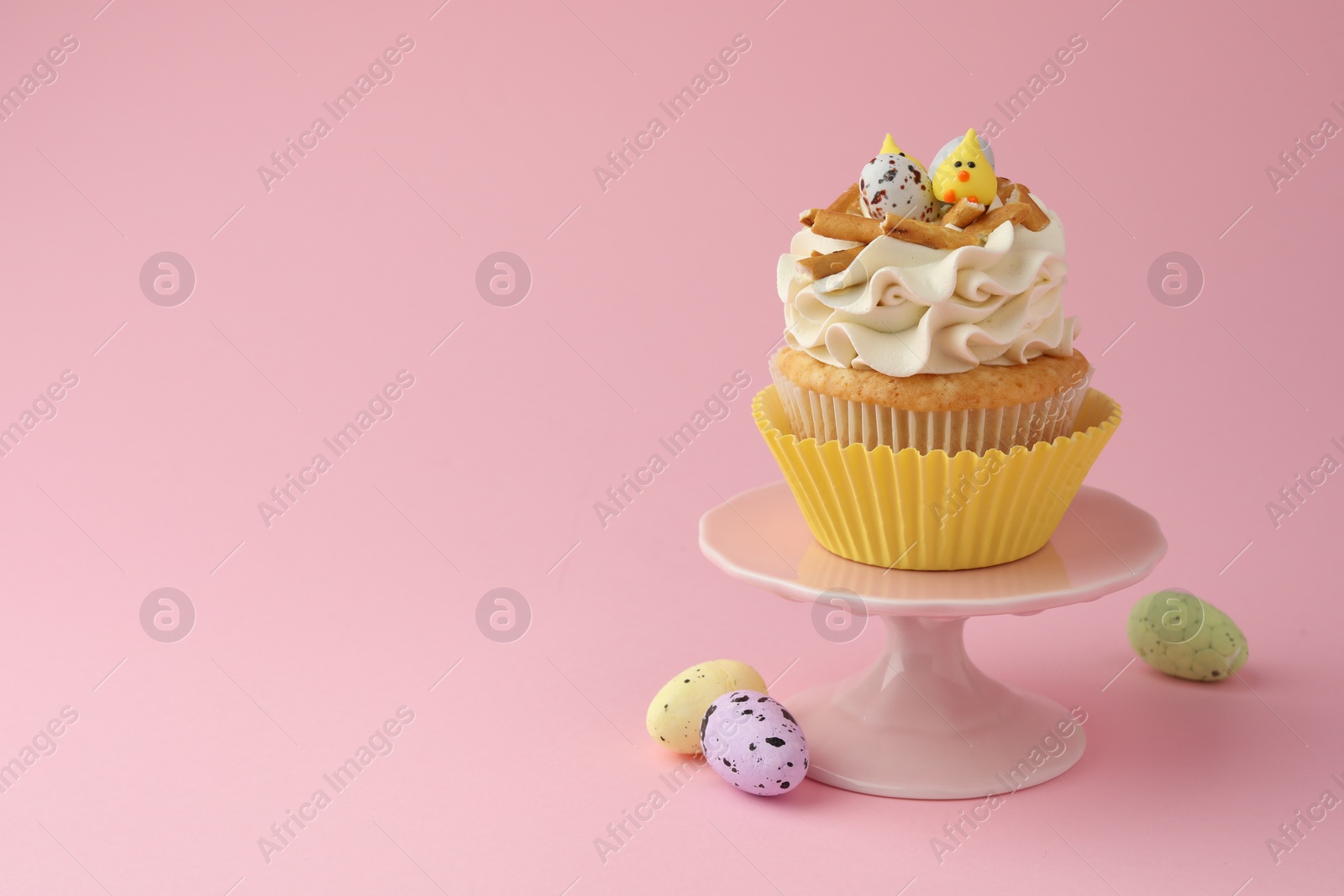 Photo of Tasty Easter cupcake with vanilla cream and candies on pink background, space for text