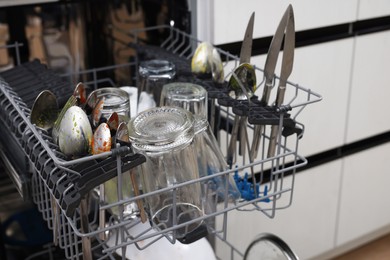 Photo of Open modern dishwasher with dirty tableware in kitchen