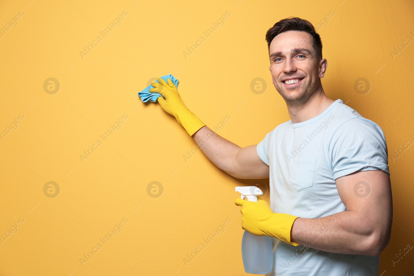 Photo of Man cleaning color wall with rag and sprayer. Space for text