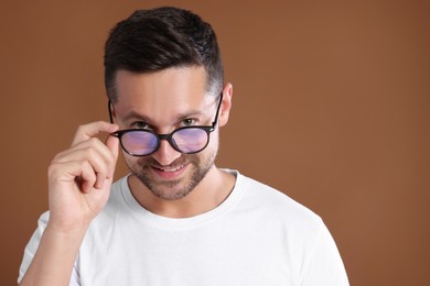 Photo of Portrait of happy man in stylish glasses on brown background. Space for text