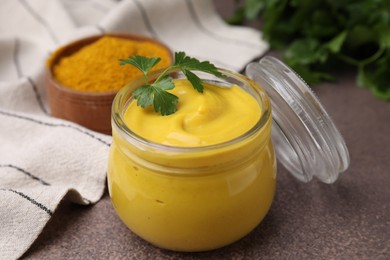 Photo of Jar with tasty curry sauce, powder and parsley on brown table, closeup