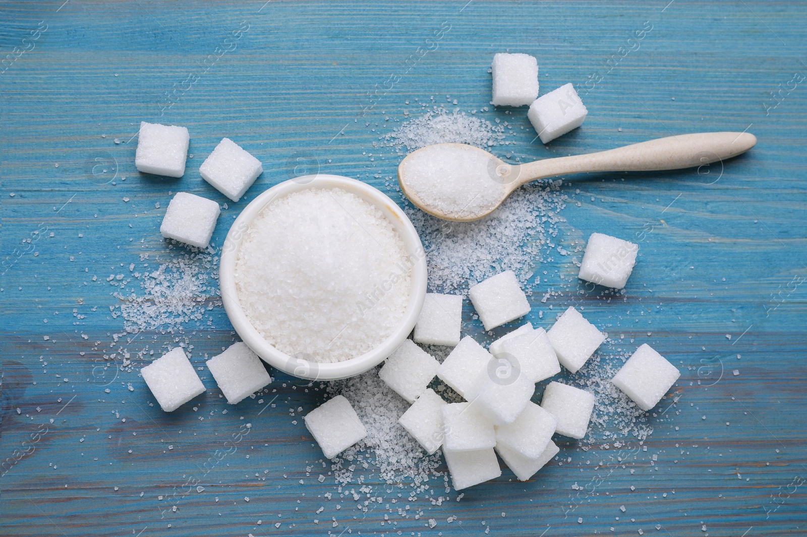 Photo of Different types of white sugar on light blue wooden table, flat lay