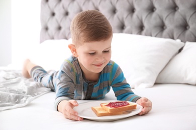 Photo of Cute little boy eating toast with sweet jam on bed