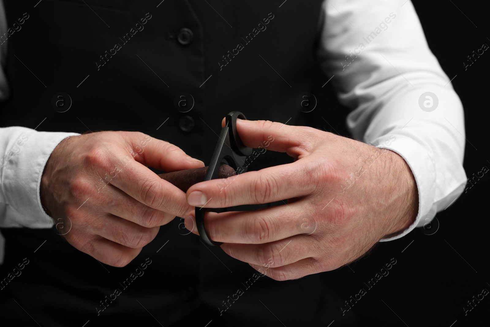 Photo of Man cutting tip of cigar on black background, closeup