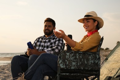 Couple with thermoses sitting in camping chairs on beach