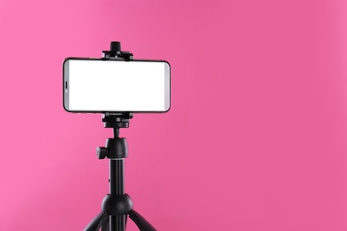 Photo of Smartphone with blank screen fixed to tripod on pink background. Space for text