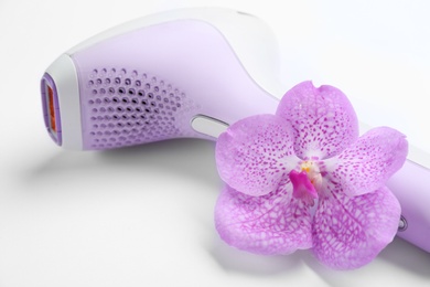 Modern photoepilator and orchid flower on white background, closeup