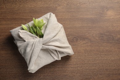 Photo of Furoshiki technique. Gift packed in white fabric decorated with beautiful flowers on wooden table, top view. Space for text