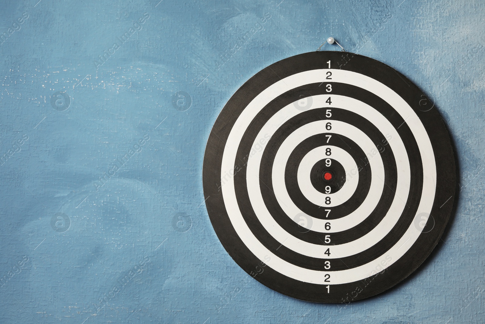 Photo of Dart board hanging on blue textured wall. Space for text