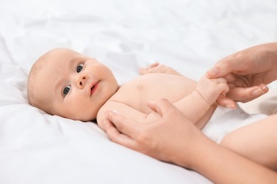 Woman applying body cream onto baby`s skin on bed, closeup