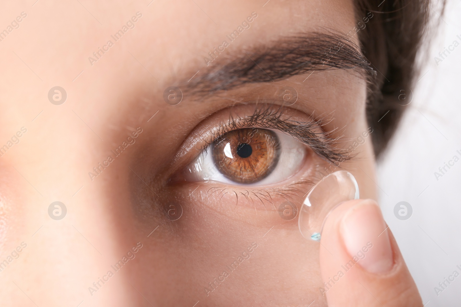 Photo of Young woman putting contact lens in her eye, closeup