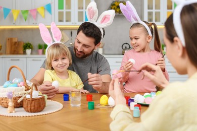 Photo of Happy family painting Easter eggs at table in kitchen