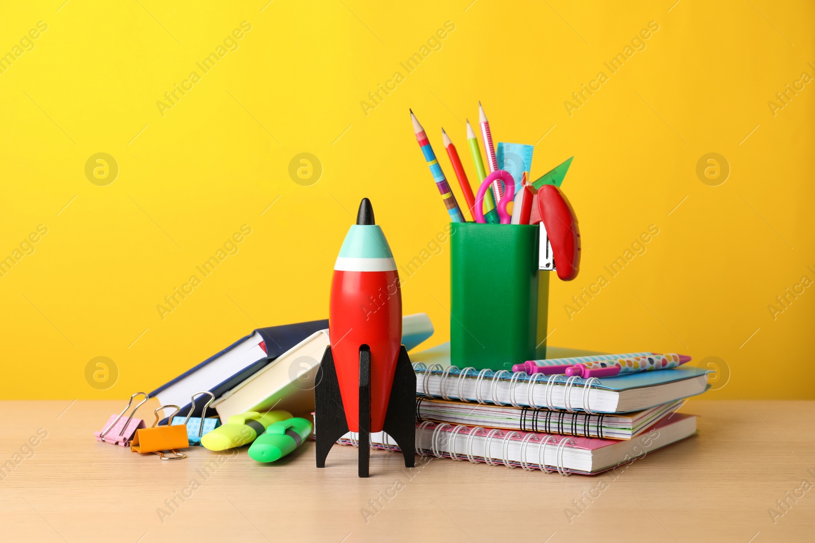 Photo of Bright toy rocket and school supplies on wooden table