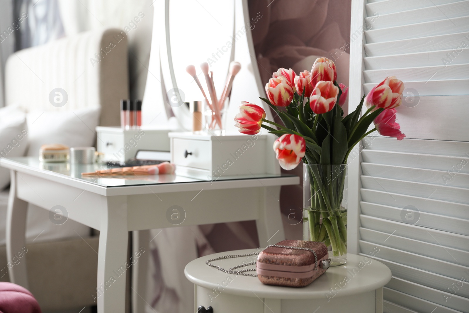Photo of Vase with tulips and stylish handbag on table indoors. Interior design