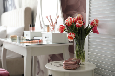 Vase with tulips and stylish handbag on table indoors. Interior design