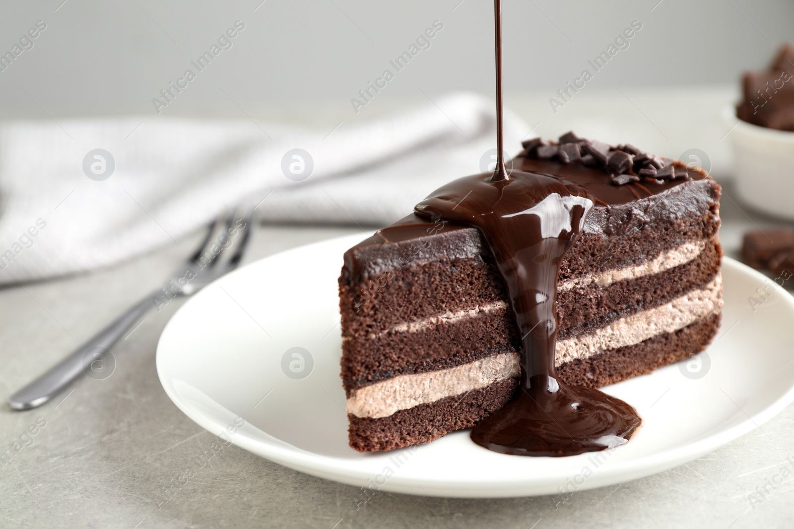 Photo of Pouring chocolate sauce onto delicious fresh cake on light table, closeup