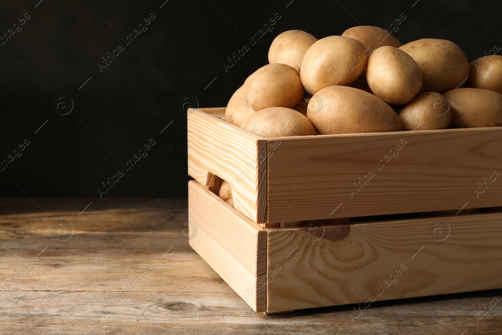 Photo of Raw fresh organic potatoes on wooden table against dark background. Space for text