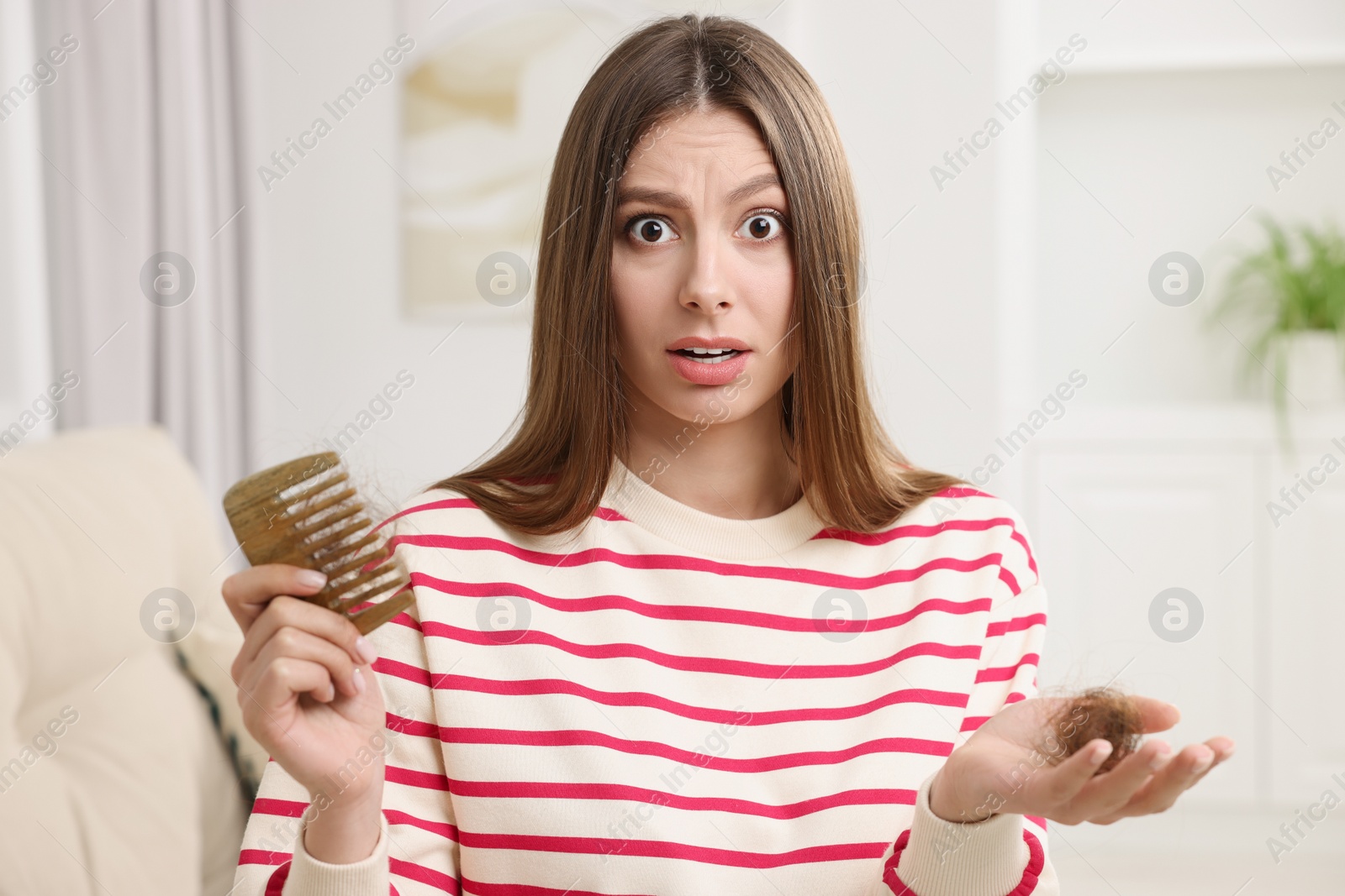 Photo of Emotional woman holding comb with lost hair at home. Alopecia problem